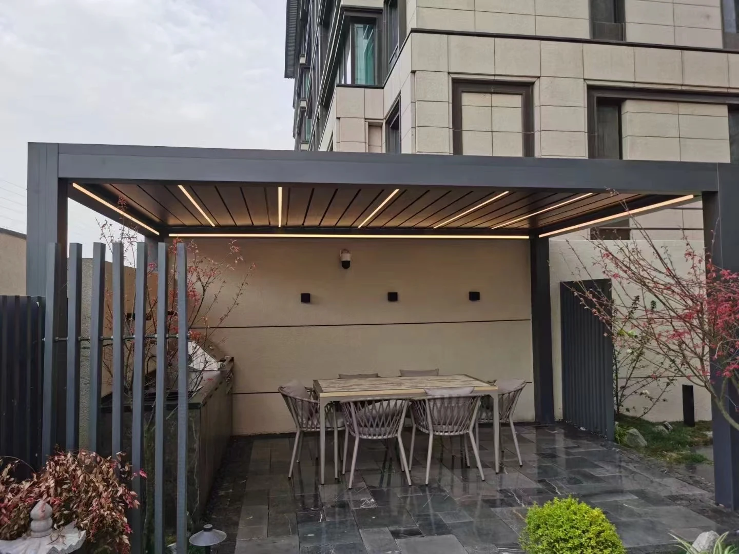 Grey pergola over a courtyard dining table with warm roof lighting