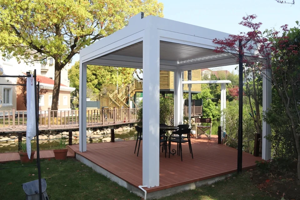 White louvre pergola on a garden deck beside trees and water